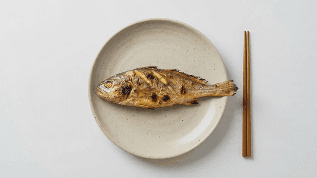 Grilled yellow croaker served on plate with chopsticks