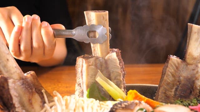김이 나는 따뜻한 갈비탕의 갈비를 집게로 꺼내는 모습