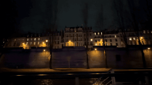 Night view of European city buildings lined up along riverbank seen from boat