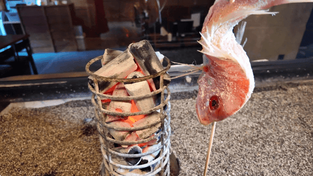 Primitive grilled fish skewered next to charcoal fire