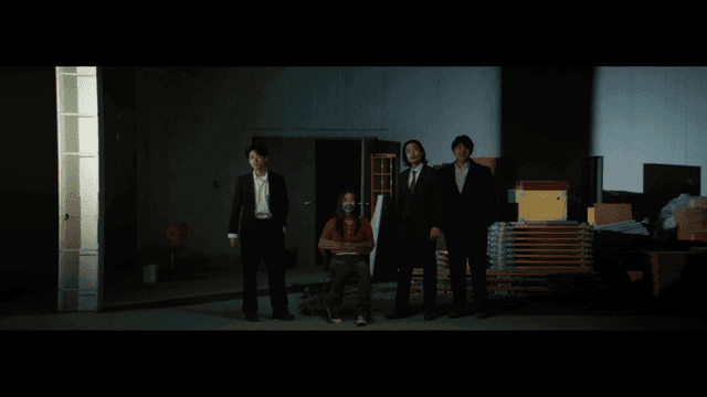 어두운 실내에서 구속된 사람을 둘러싼 정장 차림의 남성들