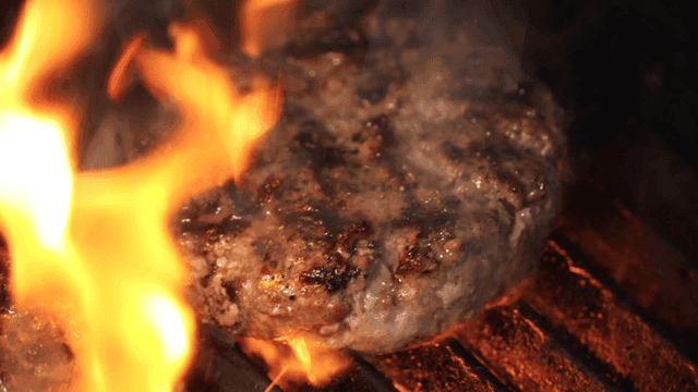 Juicy burger patty grilling over flames