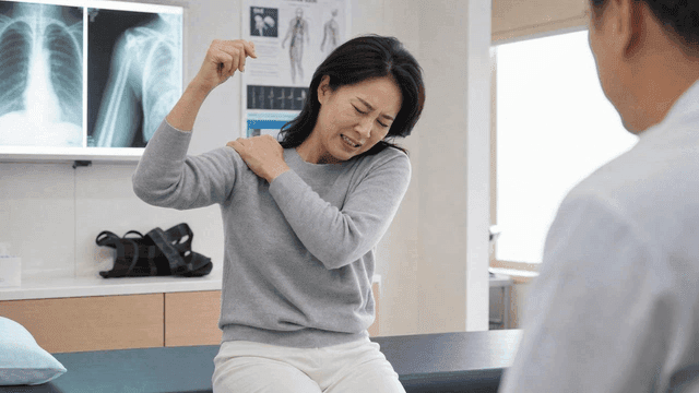 Middle-aged woman experiencing shoulder pain and back view of doctor