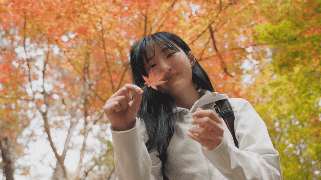 Young woman shaking autumn leaves in forest