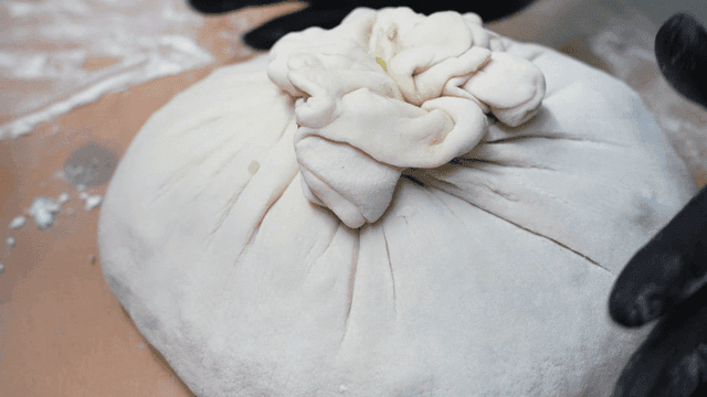 Shaping large dumpling dough with gloved hands