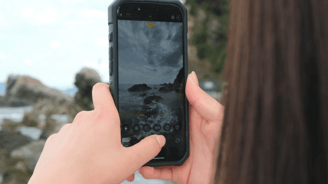 Back view of woman taking photo of rocky coastline with her cell phone