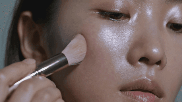 Woman applying makeup to her cheeks with brush