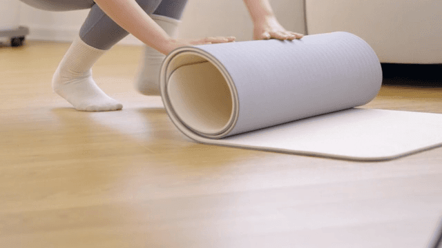 실내에서 요가 매트를 말고 있는 사람