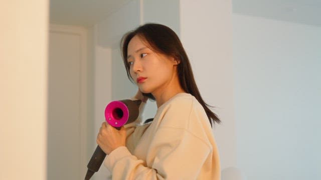 Woman drying her hair with dryer in front of a mirror