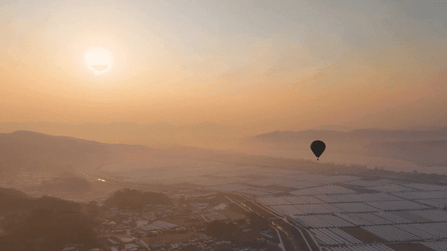 Hot air balloon flying over fields at sunrise