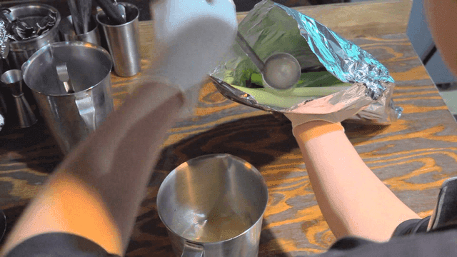 Chef pouring broth with ladle into foil with green onion