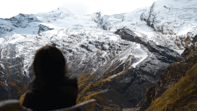 Woman sitting on bench looking out at snow-covered mountain
