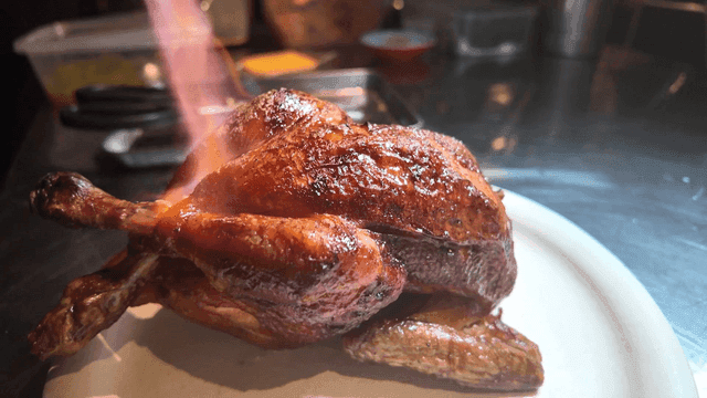 Whole chicken grilled over torch flame in kitchen
