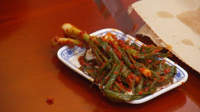 나무 테이블 위 접시에 젓가락으로 파김치를 담는 모습