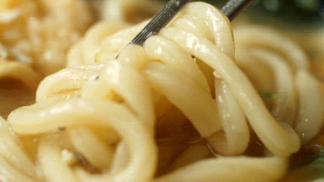 Close-up of udon noodles being lifted with chopsticks