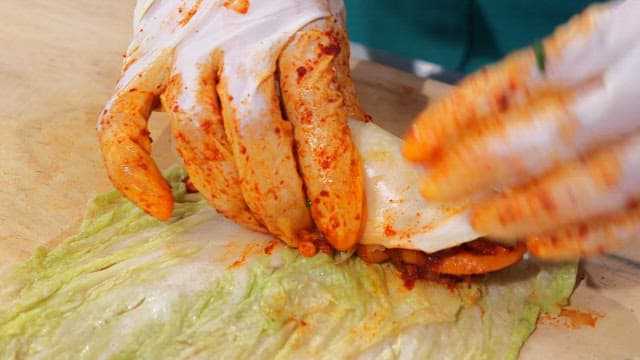 Hands wrapping sliced radish kimchi with cabbage leaves