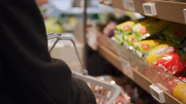 Person putting fresh vegetables into shopping cart at supermarket