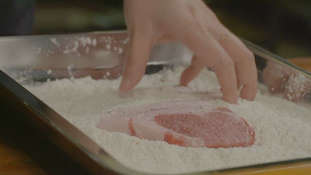 Hand coating pork with flour in a tray