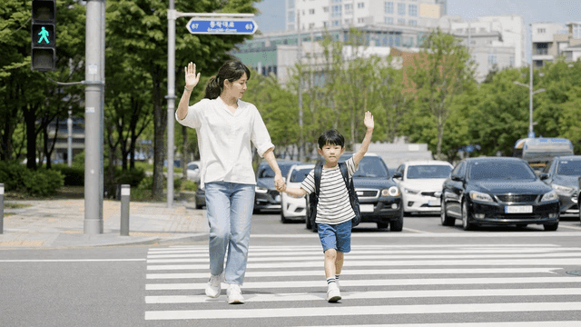 Mother and child raising their hands as they cross road at crosswalk