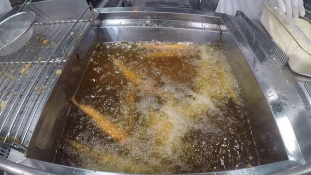 Cooking skewered sand eels from a deep fryer full of oil in a commercial kitchen