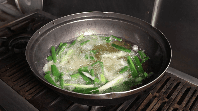 Person frying green onions in hot oil