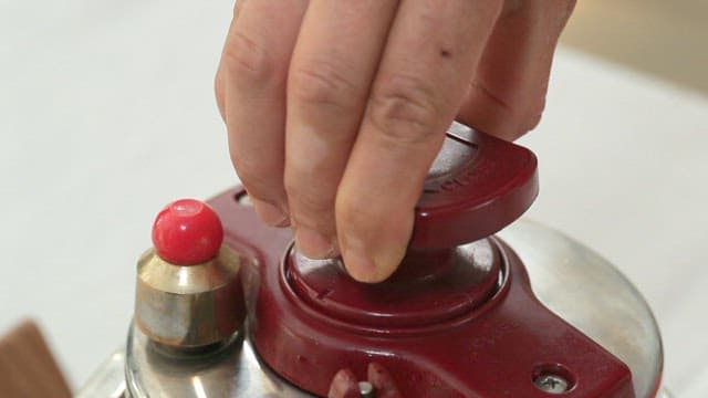 Hand turning the knob of a pressure cooker with brown rice