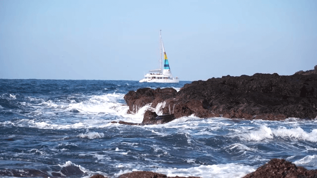 Waves crashing on rocks with a yacht