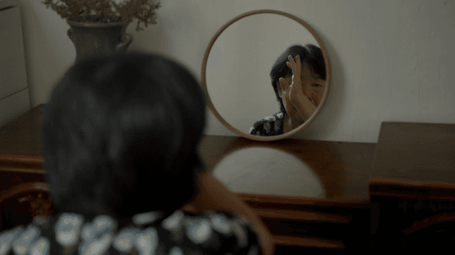 An elderly woman adjusting hair in front of a mirror