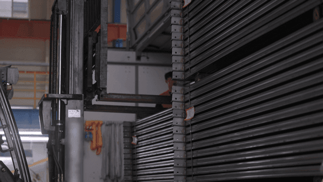 공장에서 금속 빔을 옮기는 지게차