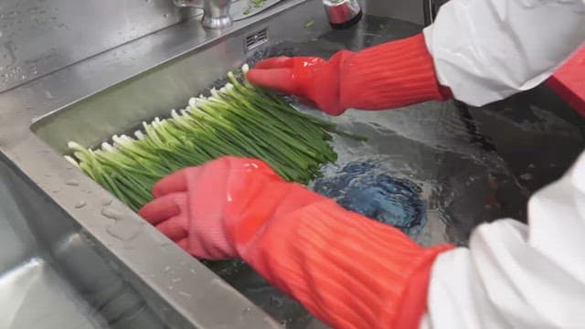 Washing green onions in a sink with rubber gloves