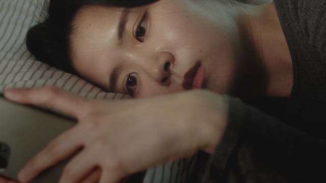침대에 누워 휴대폰을 바라보는 여자
