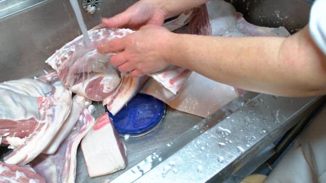 Washing large cuts of raw meat under running water in a kitchen