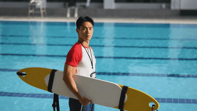 Lifeguard holding a rescue board by the pool