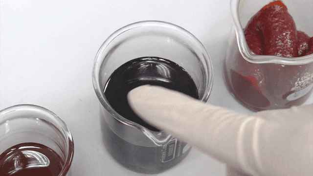 Seasoning sauces in a beaker beside a gloved hand