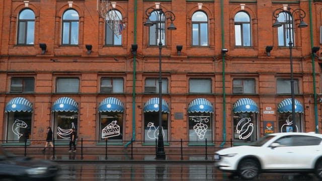 Cars and pedestrians passing by on the road in front of a restaurant on a rainy afternoon