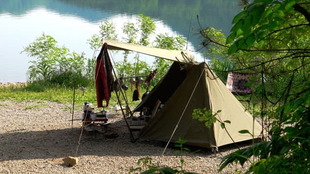 Campsite next to a lake with camping gear and tents set up on a sunny day