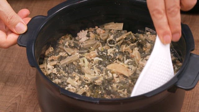 Stirring a generous amount of dried radish greens rice in a rice cooker with a spatula