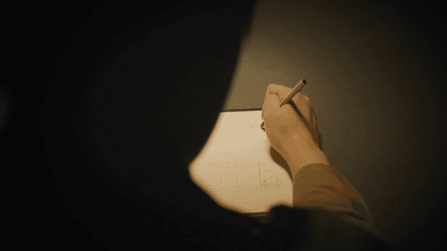 Person writing notes in a dimly lit room