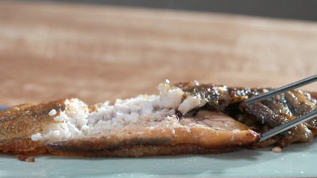 Grilled fish being eaten with chopsticks indoors