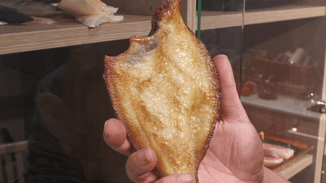 Hand holding grilled fish in front of shelf