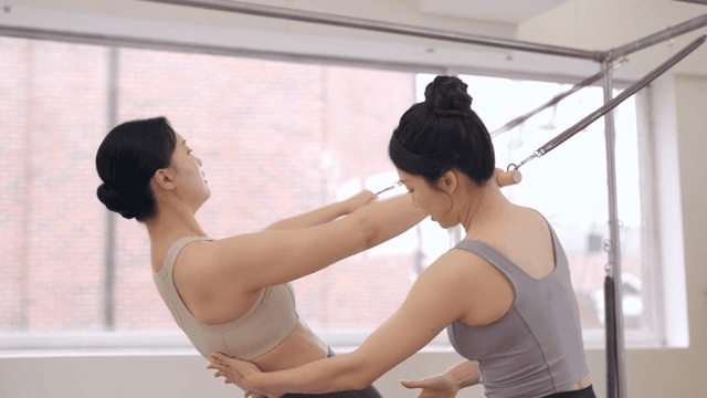Pilates instructor assists a student indoors