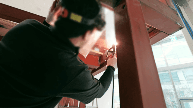 Worker welding metal beam indoors