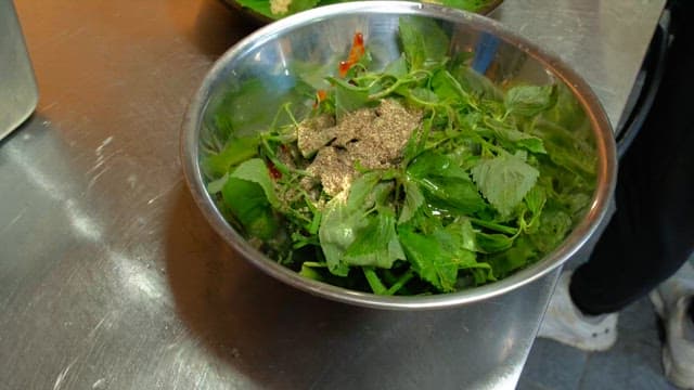 Mixing steamed meat and vegetables with seasoning in a metal bowl