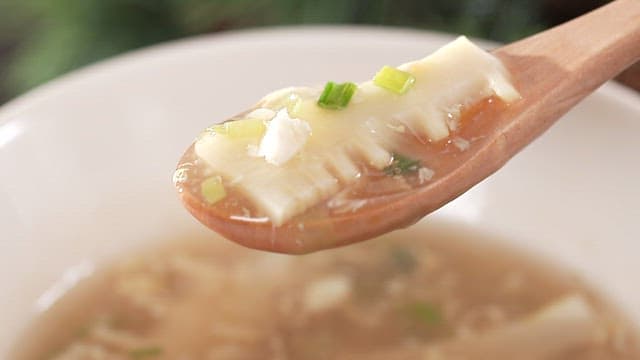 Wooden spoon stirring warm soup with bamboo shoots