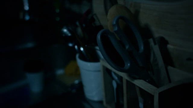 Hand Picking Scissors up from a Pencil Holder on a Table in a Dark Room