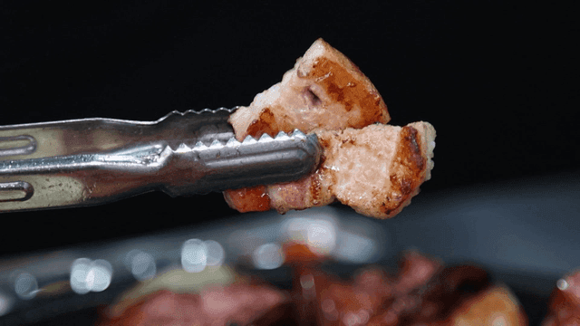 Grilled pork belly held with tongs
