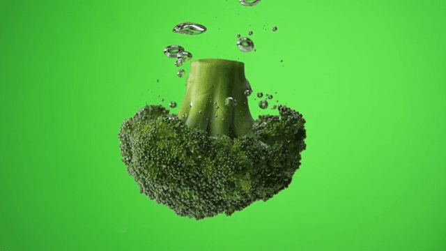 Broccoli falling into water creating bubbles on green background