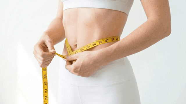 Woman measuring her waist circumference with measuring tape
