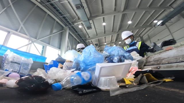 Plastic waste sorting process in a recycling plant with workers wearing safety gear