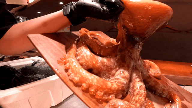Chef lifting octopus with suction cups attached to cutting board